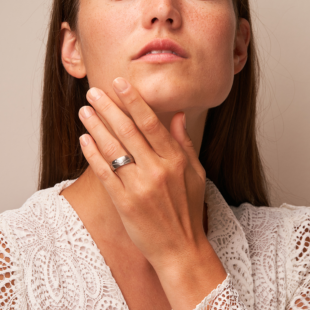 Seidenmatte Stahl Eheringe mit 3 Diamanten und zierlicher Fuge auf Hand am Gesicht