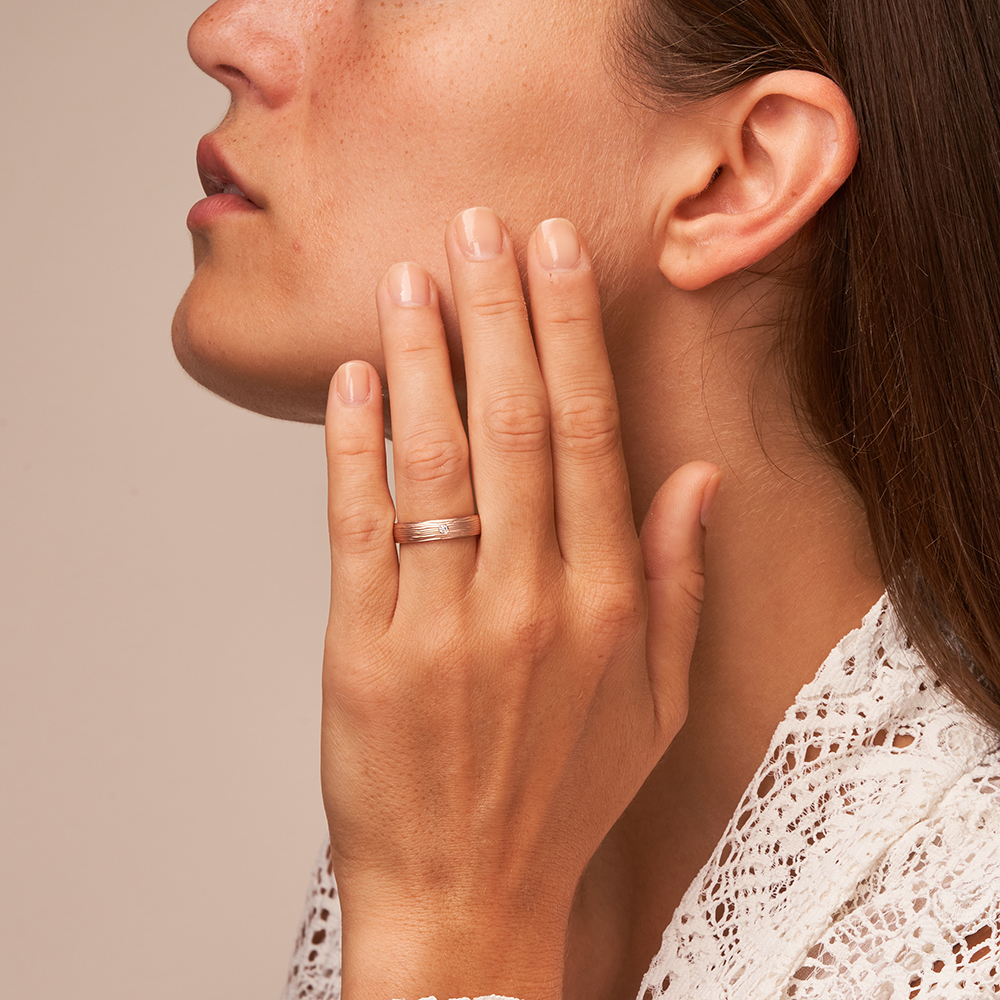 	Eheringe aus matt strukturiertem Roségold mit Diamanten auf Hand im Gesicht