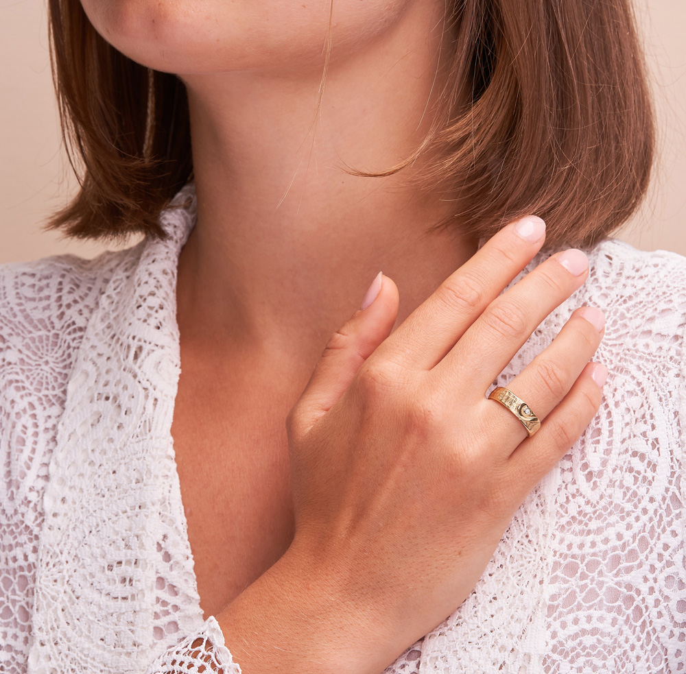 Aufnahme von strukturierten Trauringen aus Gelbgold mit Herzmuster und Diamant im Herz auf Hand