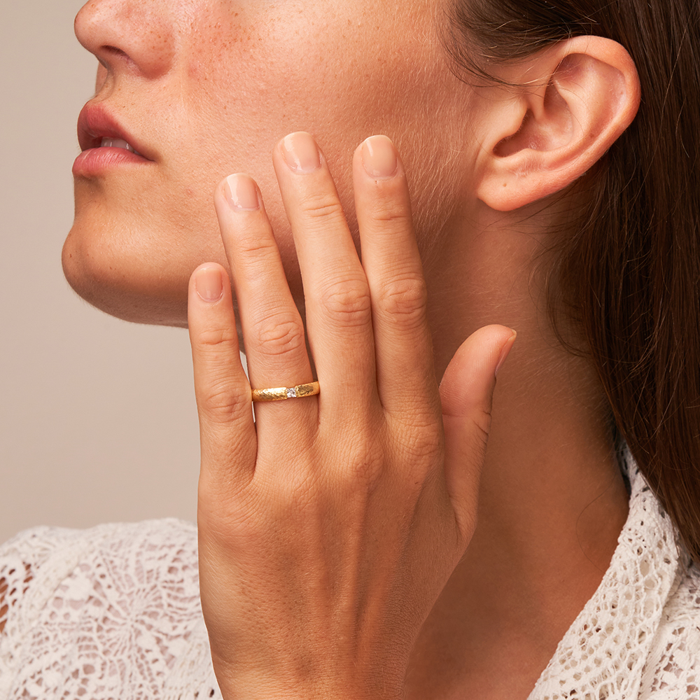 Mattierte strukturierte Eheringe aus Gelbgold mit Diamanten und Hammerschlag auf Hand im Gesicht