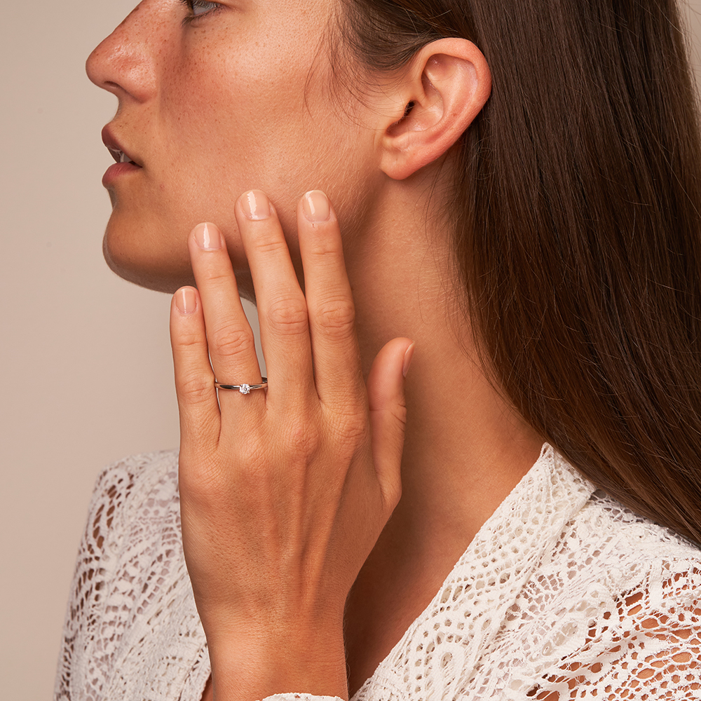 Platin Verlobungsring mit 0.15 Karat Diamant auf Hand am Gesicht