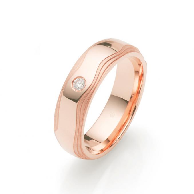 Aufnahme von stufig gestalteten Roségold Trauringen mit sandmatten Rändern und Diamanten