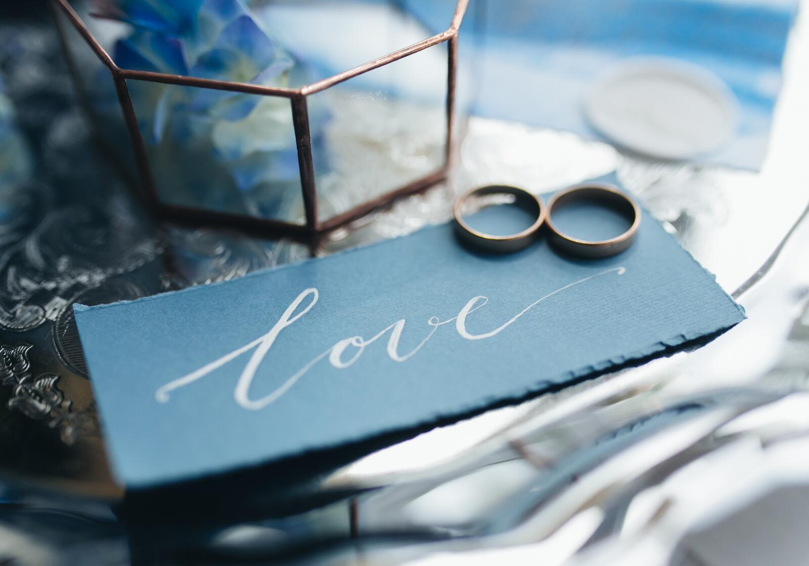 Multifunktionale Eheringe liegen auf einer blauen Karte mit Aufschrift - love