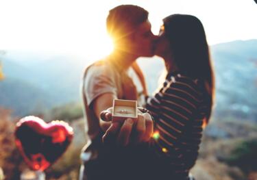 Paar küsst sich und hält Verlobungsring in Kamera